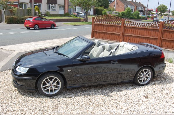 A black Saab convertible with the roof down on the forecourt