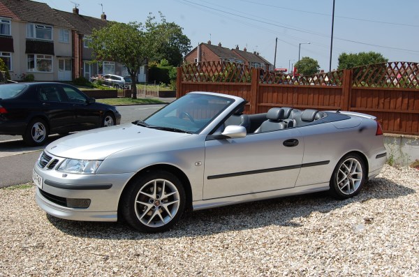 A silver convertible with the roof down beside the fence