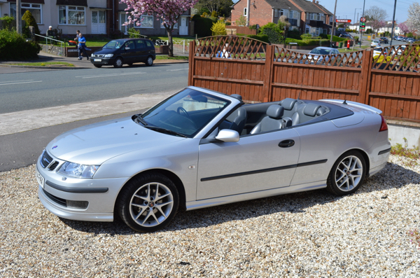 A silver Saab convertible with the roof down on the gravel forecourt