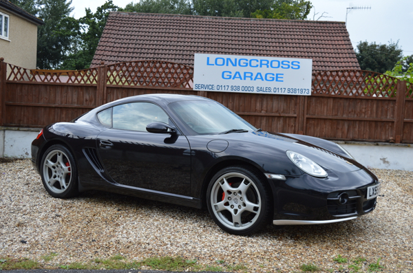 A black coupe on the gravel in front of the Longcross Garage sign