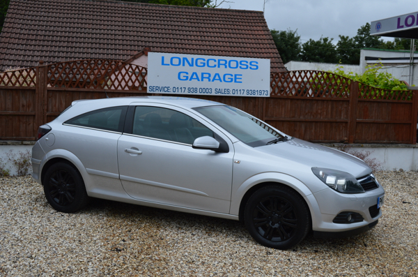 A silver Vauxhall three-door with black wheels in front of the Longcross Garage sign