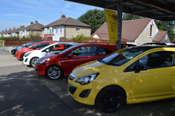 A yellow hatchback and a line of cars under the Longcross Garage canopy