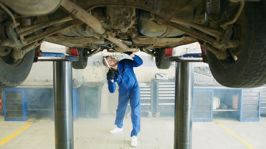 A mechanic in blue overalls checking a car raised on a lift