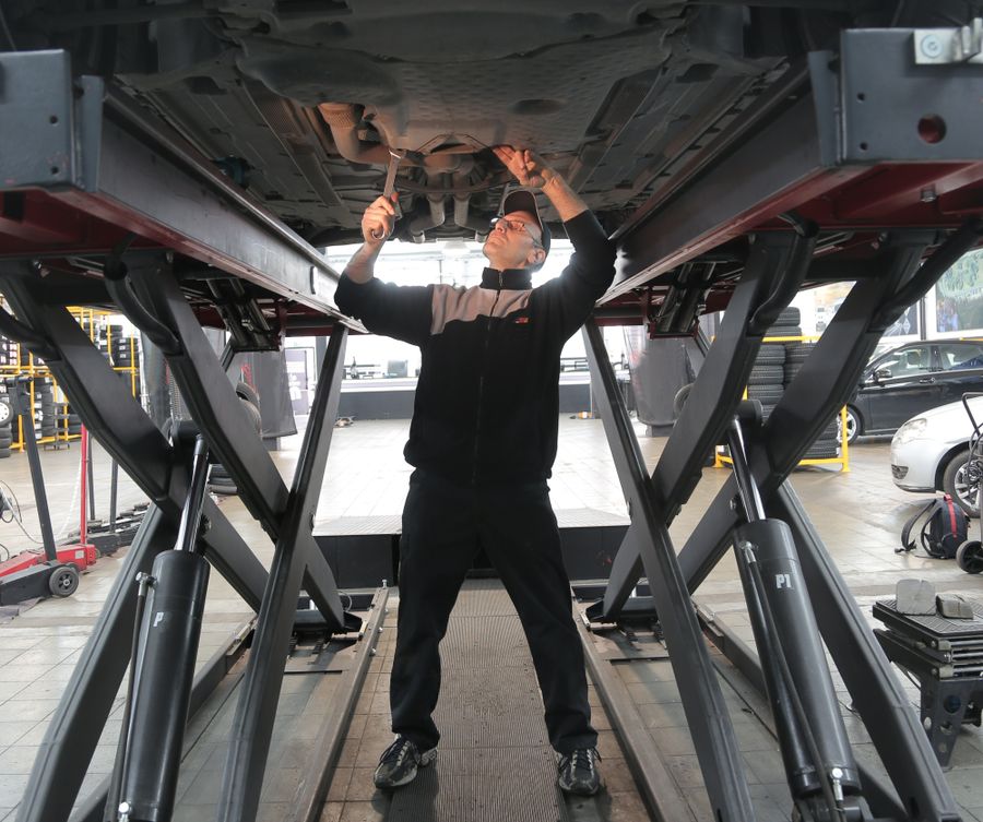 A mechanic underneath a car on a lift, checking the underside