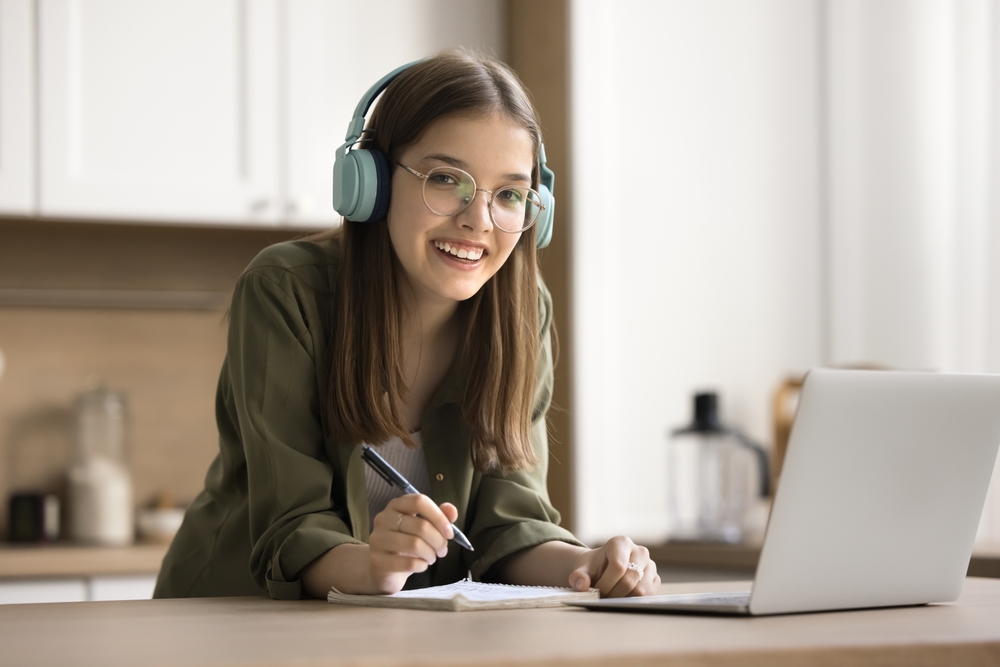 cheerful teenage girl working online with a laptop and wearing headphones.