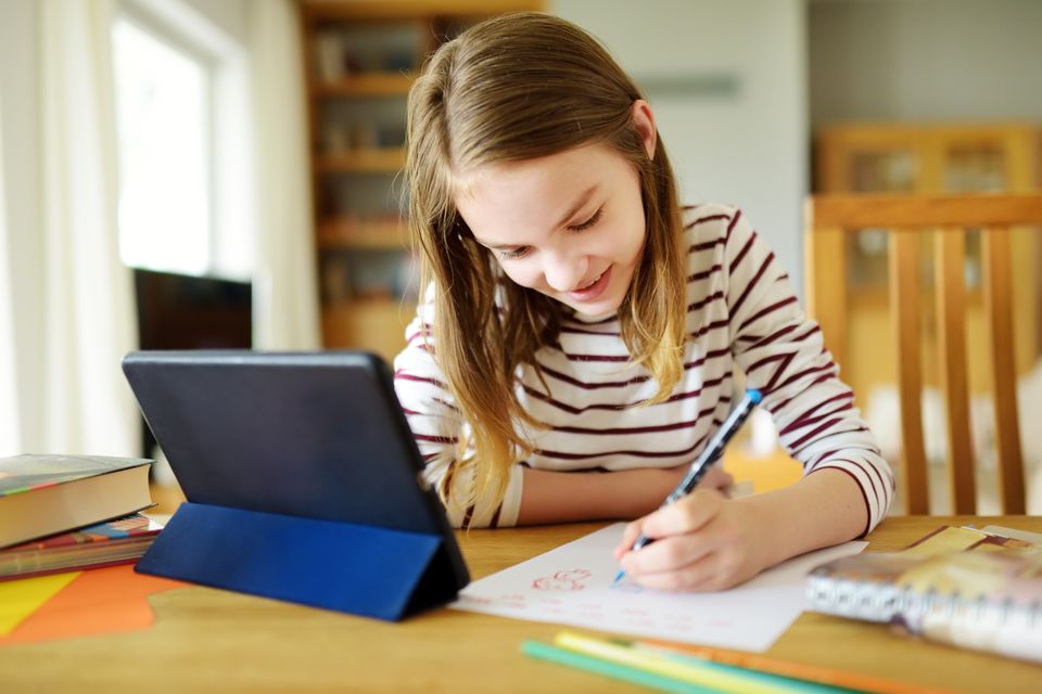 A girl drawing and writing at a desk beside her tablet