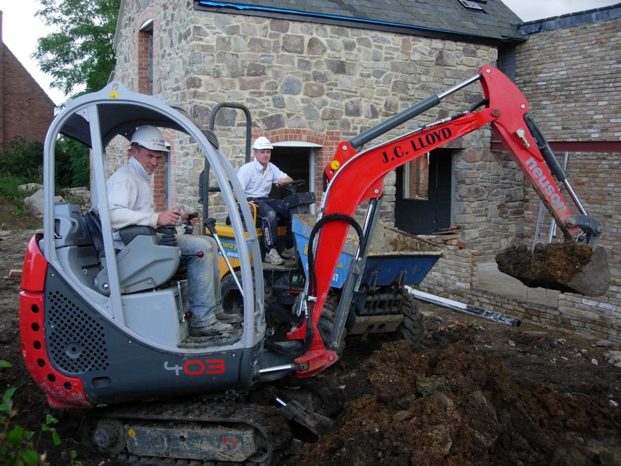 One man controlling a mini-digger and another man sitting on a tipper truck