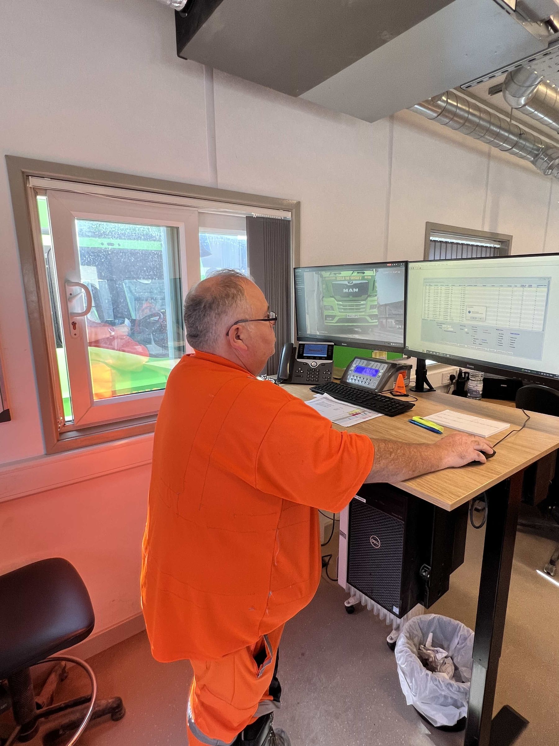 A plant operator in hi-vis at the control desk, watching the plant on a bank of screens
