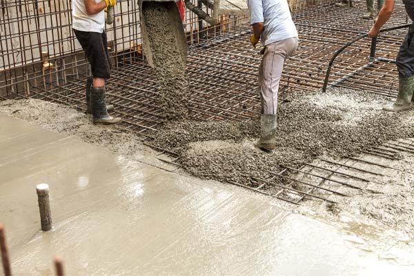Workers in wellingtons spreading a concrete floor over its reinforcement