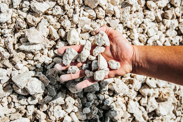 A hand holding pale crushed limestone over a heap of the same stone