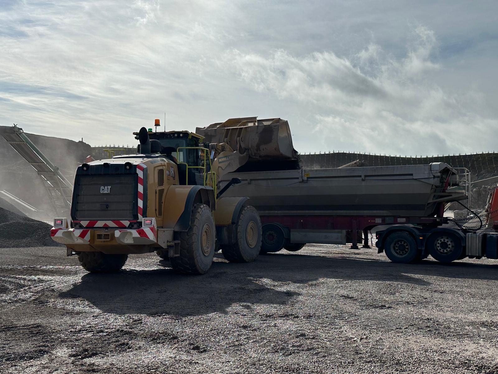 A loading shovel filling a tipper lorry beside the stockpiles