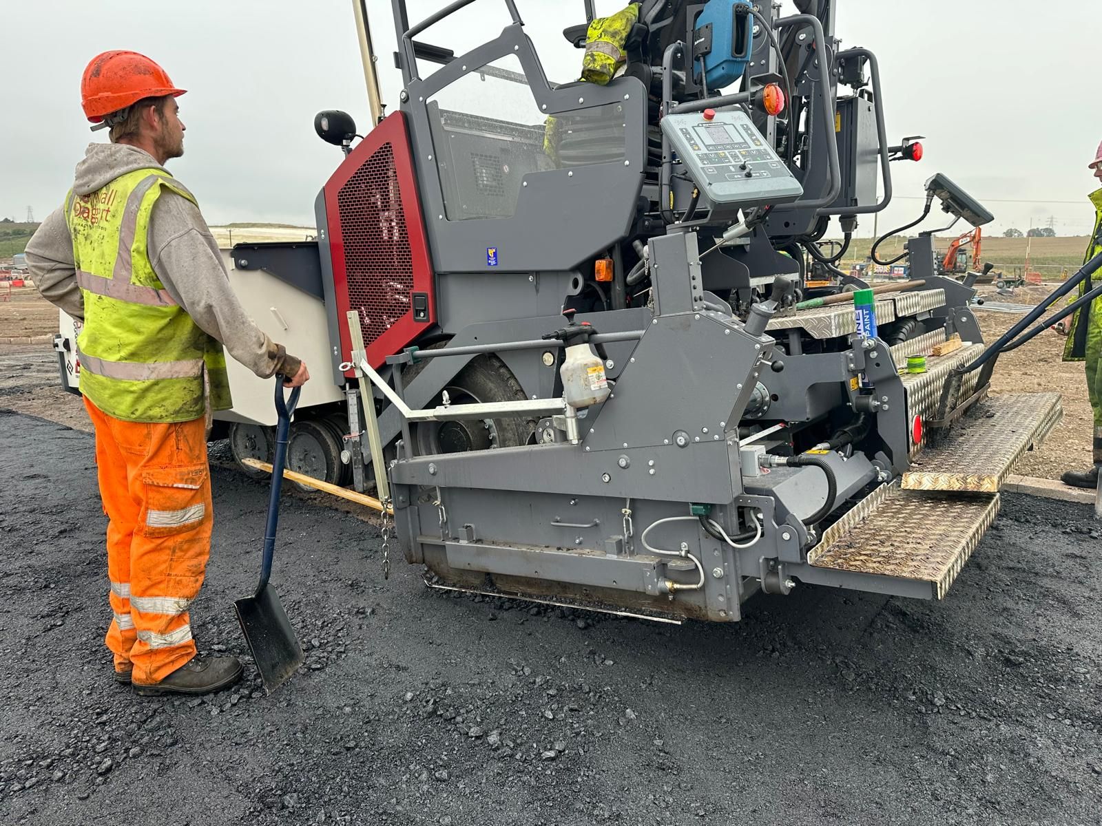 A paving crew in hi-vis beside an asphalt paver laying a fresh surface