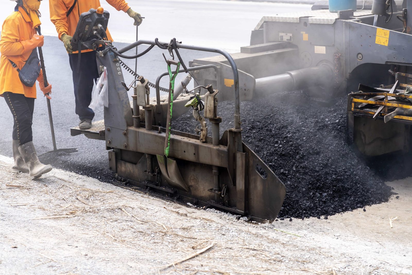 A paving crew in orange working beside an asphalt paver