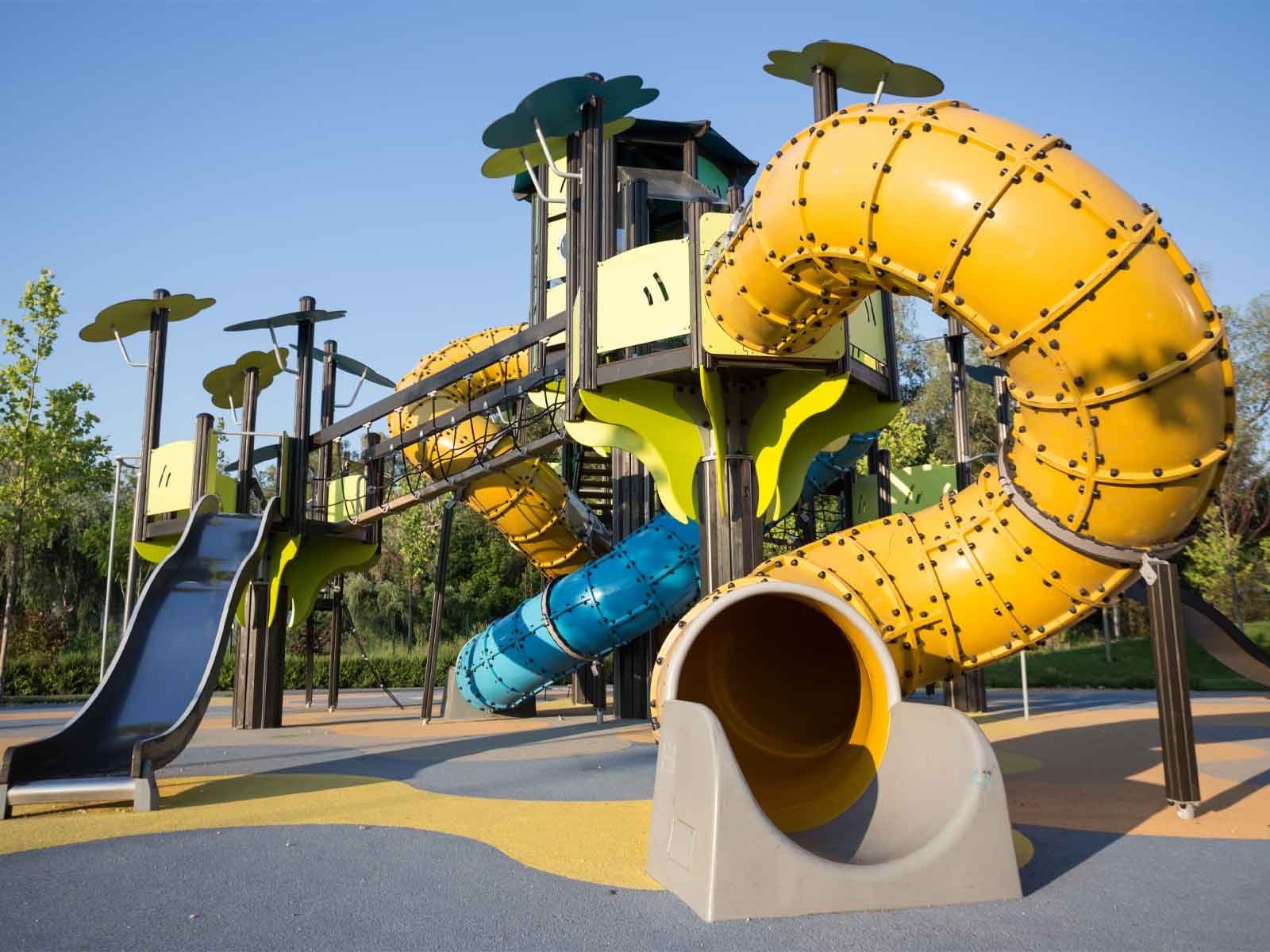 A playground with a yellow tube slide, set on an asphalt surface