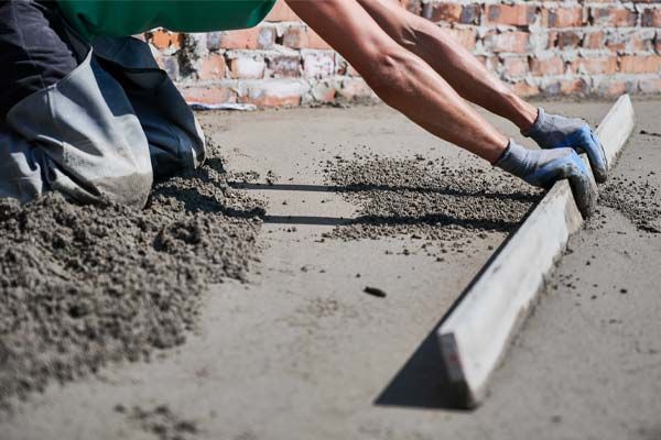 A worker levelling a fresh concrete base with a straight edge