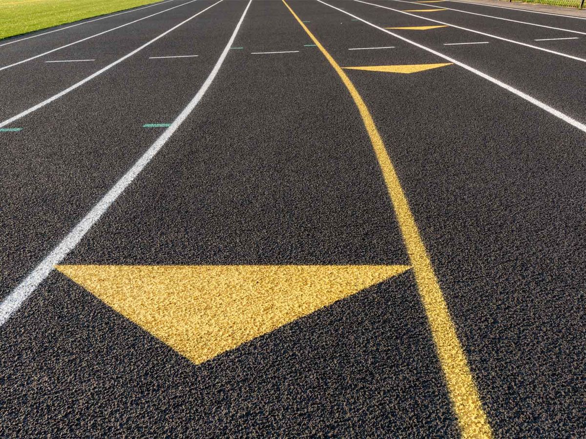 Lanes of a dark asphalt running track marked in white and yellow
