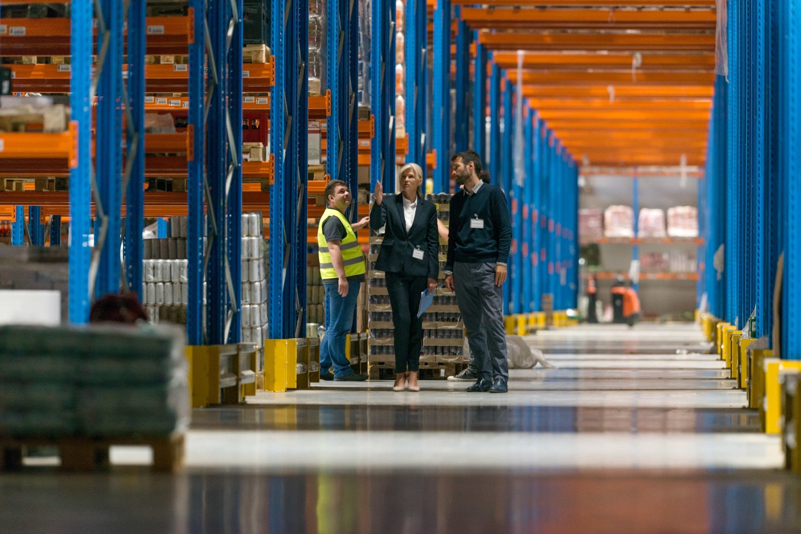 Warehouse staff talking between tall blue and orange racking